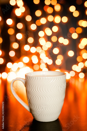 White mug on the dark brown table and background with golden bokeh. Christmas holiday concept