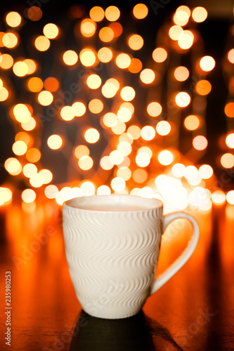 White cup of cocoa on the dark brown table and background with golden bokeh. Christmas holiday concept