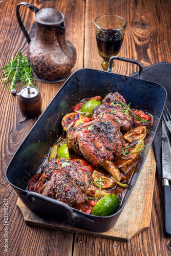 Traditional barbecue leg of lamb with lemon and tomatoes as closeup in an old skillet