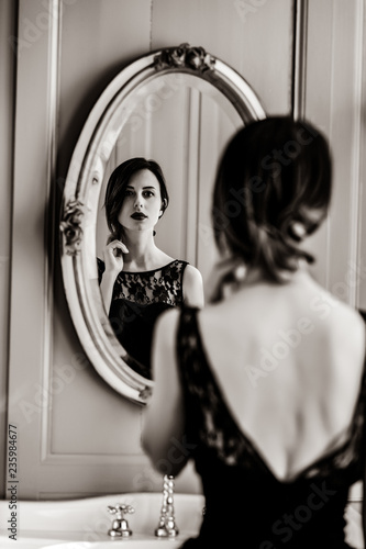 portrait of beautiful young woman looking at herself in the wonderful mirror . Image in black and white color style