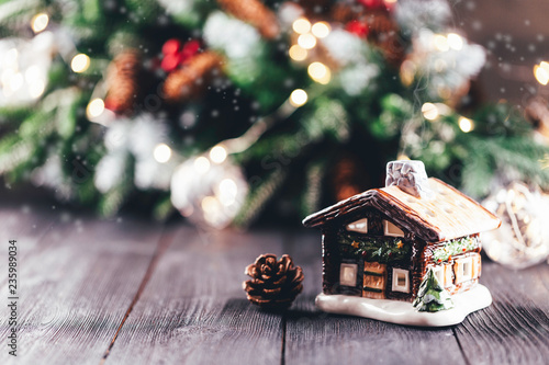 Christmas village house with candle inside on rustic table with christmas tree in the background, bokeh lights, snow and smoke effect, copy space