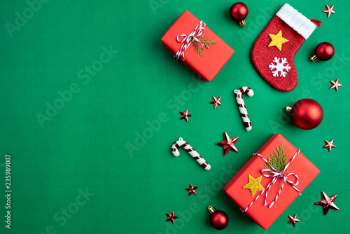 Christmas background concept. Top view of Christmas green and red gift box with socks decoration, spruce branches, pine cones, red berries and bell on green background.