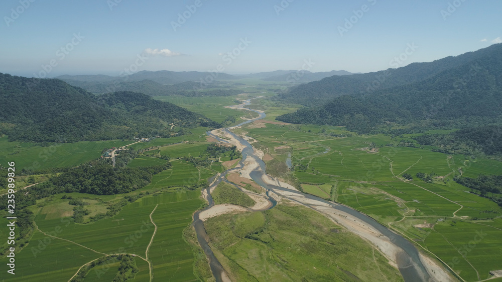 Mountain valley with river, farmland, rice fields. Aerial view of Mountains with green tropical rainforest, trees, jungle with blue sky. Philippines, Luzon.