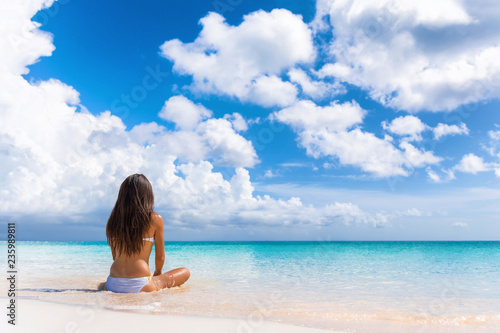 Beach luxury travel woman relaxing on summer vacation at spa retreat resort sitting enjoying ocean view meditating. Wellness relaxation holiday.