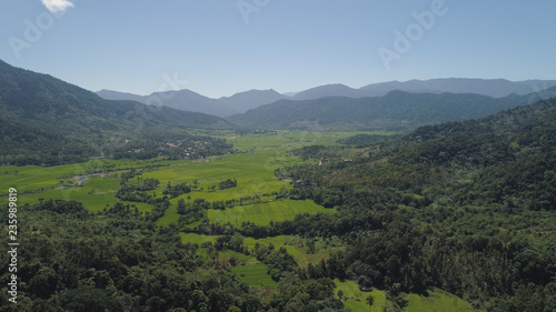 Mountain valley with village, farmland, rice fields. Aerial view of Mountains with green tropical rainforest, trees, jungle with blue sky. Philippines, Luzon.
