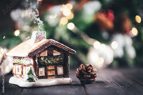 Christmas village house with candle inside on rustic table with christmas tree in the background, bokeh lights, snow and smoke effect, copy space