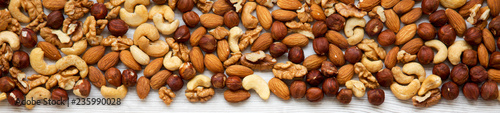 Assorted mixed nuts (cashew, hazelnuts, walnuts, almonds) on white wooden surface, overhead view. From above.