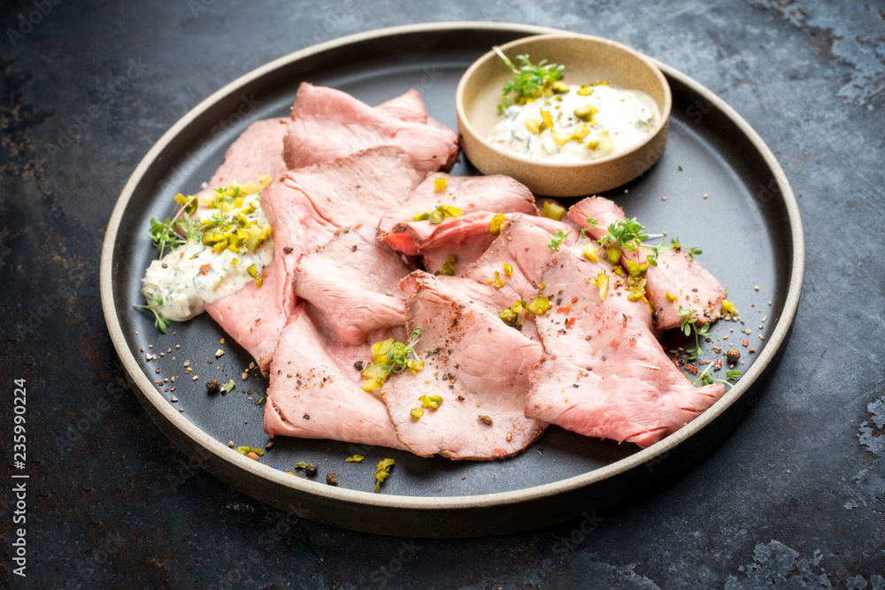Traditional lunch meat with sliced cold cuts roast beef and remoulade as closeup on a modern design plate on black background Traditional lunch meat with sliced cold cuts roast beef and remoulade as closeup on a modern design plate on black background