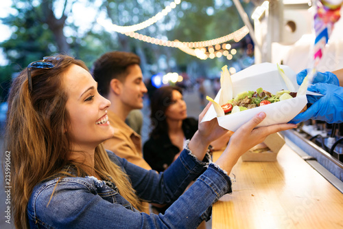 Group of attractive young friends choosing and buying different types of fast food in eat market in the street.