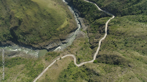Aerial view of mountain river in the cordillera, road on the slopes, mountains covered forest, trees. Cordillera region. Luzon, Philippines.