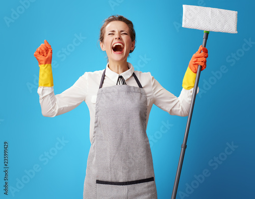 happy young cleaning woman in apron on blue with mop rejoicing photo