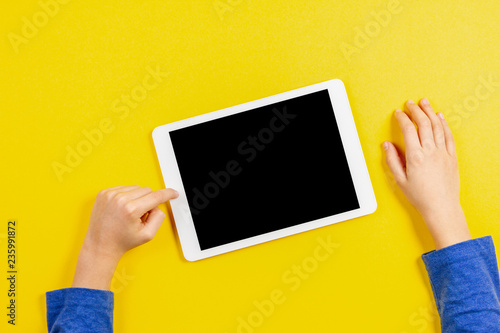Kid hands with tablet computer on yellow background