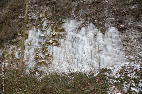 Icicles of an overfrozen spring dripping down a limestone cliff