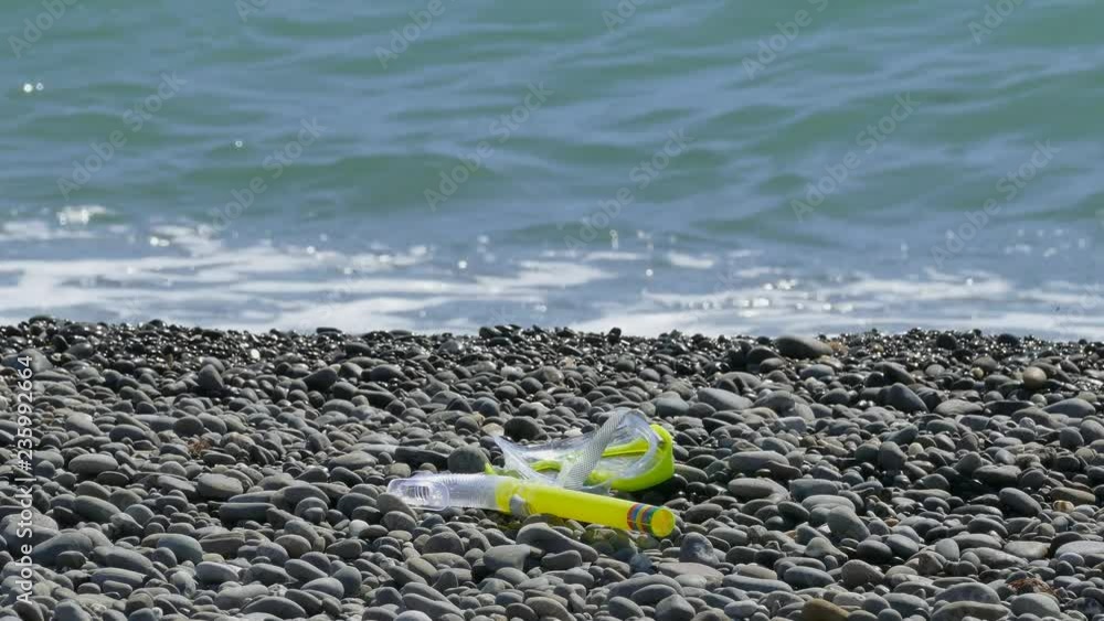 mask and snorkel are on the shore. Waves breaking on a pebble beach. mask and snorkel are on the shore. Waves breaking on a pebble beach.