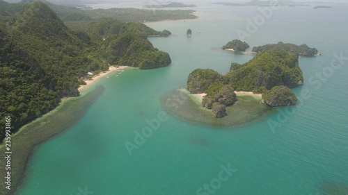 Aerial view of island Kagbalinad with sand beach and turquoise water in blue lagoon among coral reefs, Caramoan Islands, Philippines. Mountains covered with tropical forest.