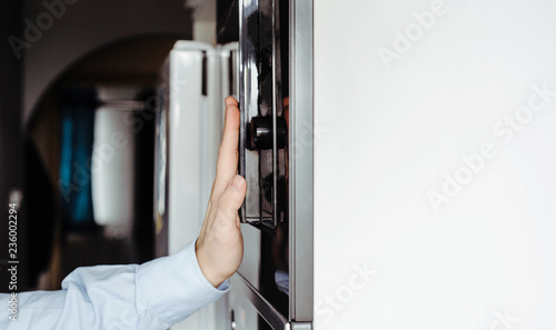 A man dressed in a business shirt puts a dish into the oven and microwave. Concept of cooking by men, turning on the oven for preparing meals. Men cooking at home, using an oven.
