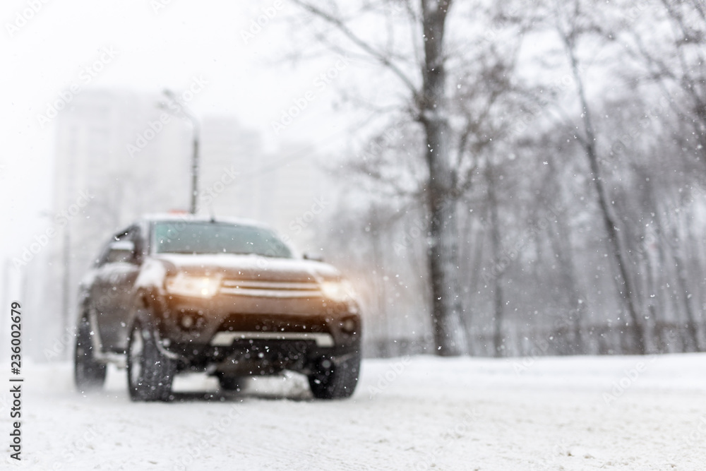 Heavy snowfall and blurred SUV awd car on road. 4wd vehicle on city street at winter. Seasonal roadside assistance concept. Copyspace Heavy snowfall and blurred SUV awd car on road. 4wd vehicle on city street at winter. Seasonal roadside assistance concept. Copyspace