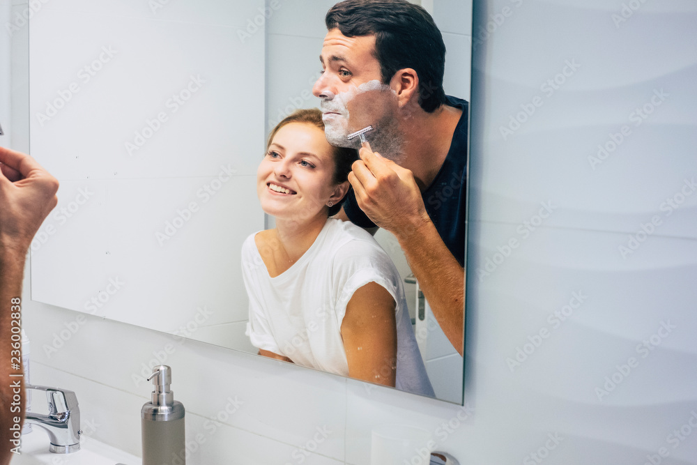 Young millennial couple in love at home prepare to go work at office - man cut the beard and woman look at him smiling - happiness for life together - morning getting ready for people Young millennial couple in love at home prepare to go work at office - man cut the beard and woman look at him smiling - happiness for life together - morning getting ready for people