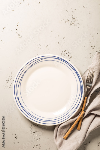 Empty white plate, napkin and cutlery on grey stone background