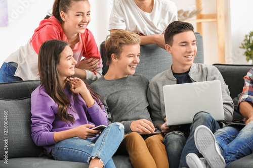 Group of teenagers with modern devices sitting on sofa indoors