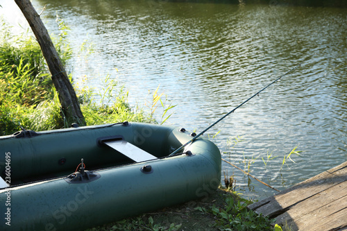 Inflatable boat with rod for fishing near wooden pier at riverside