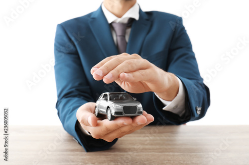 Insurance agent holding toy car in hands over table against white background