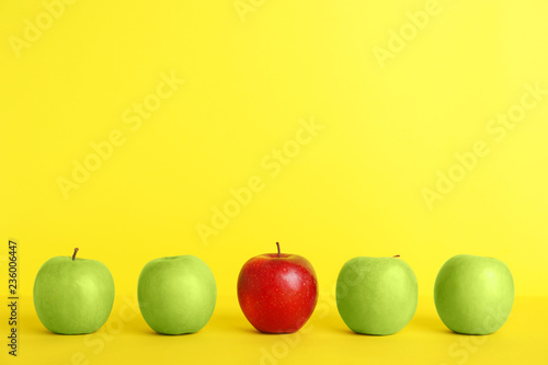 Row of green apples with red one on color background. Be different