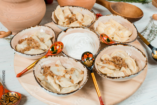 dumplings with cheese and potatoes and sour cream on a wooden board on white tablr traditional russian boiled food photo