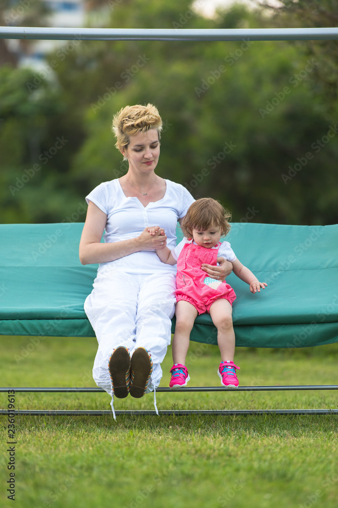 Fototapeta premium mother and little daughter swinging at backyard