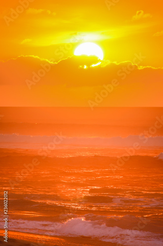 Orange sun setting over waves on Sunset Beach on the north shore of Oahu, Hawaii, USA