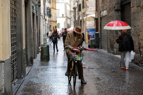 Italian man riding his bike through a cobble stoned village hold a red umbrella #4