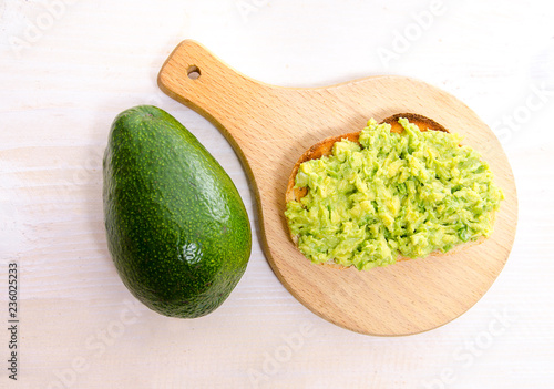 Top view avocado toast on wooden cutting board next to fresh avocado 
