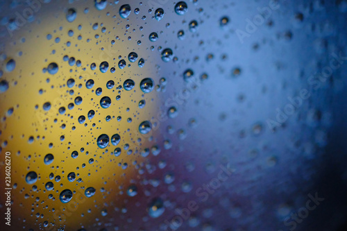 Rain drops on glass window at night in yellow and blue tone .