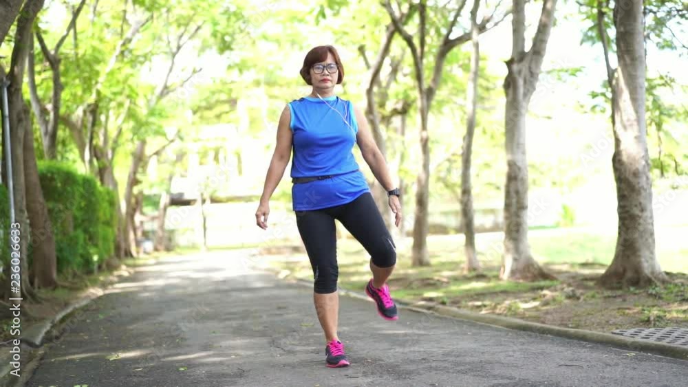 Senior asian woman stretch thigh muscles at park and listening to music. Athletic senior exercising together outdoor. Fit senior runners stretching before running outdoors. Senior asian woman stretch thigh muscles at park and listening to music. Athletic senior exercising together outdoor. Fit senior runners stretching before running outdoors.
