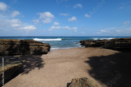 Playa El Coco, Nicaragua, on a sunny summer day showing its beach, rocks, vegetation and cloudscape.