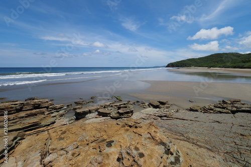Playa El Coco, Nicaragua, on a sunny summer day showing its beach, rocks, vegetation and cloudscape.