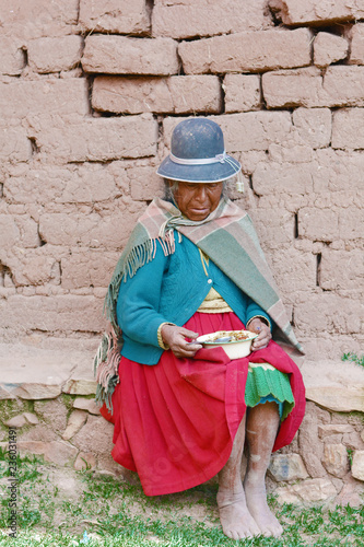 Native american old woman in traditional aymara clothes eating outside.