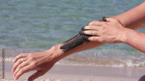 the girl begins to smear her hand with therapeutic mud, on the background of sea beach photo