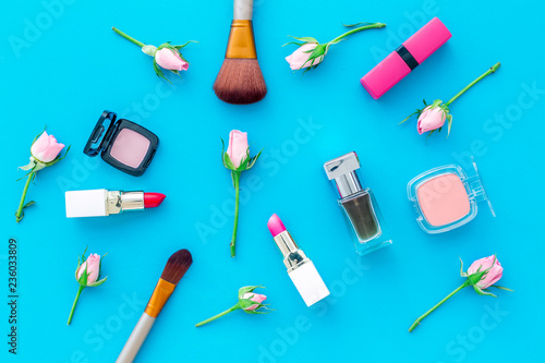 Decorative cosmetics layout. Pink tones of lipstick, bulk, eyeshadow, perfume, brushes among rose flowers on blue background top view