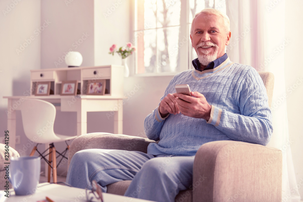 Smiling old man spending time with smartphone