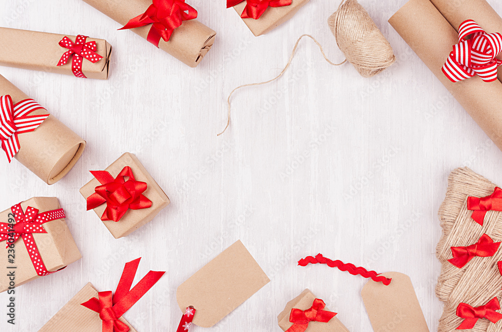 Christmas preparations - packaging gifts boxes in kraft paper with red bows and ribbons, twine on white wood table, frame, copy space. Christmas preparations - packaging gifts boxes in kraft paper with red bows and ribbons, twine on white wood table, frame, copy space.