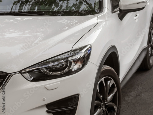  Parked white car front headlight and wheel view standing on street parking lot.