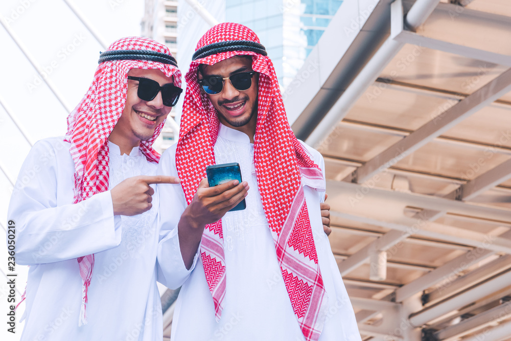 Two Arab businessmen messaging on a mobile phone in city