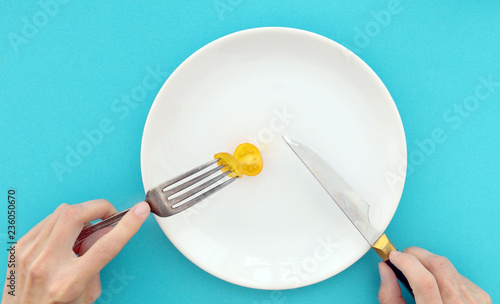 Woman on a diet eats yellow tomato. Female hands with cutlery and empty plate on turquoise background top view, dieting concept