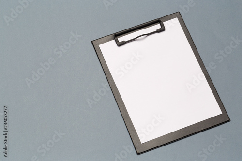 Black clipboard with empty sheets of paper on a dark table