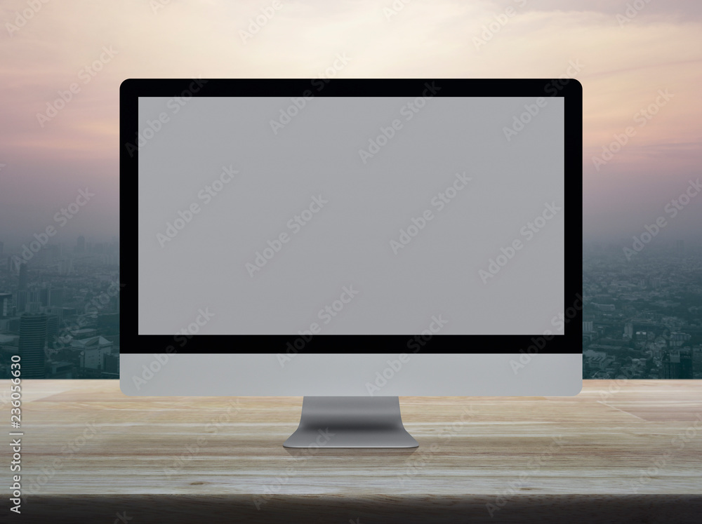 Fototapeta premium Desktop modern computer monitor with grey wide screen on wooden table over modern city tower and skyscraper at sunset sky, vintage style