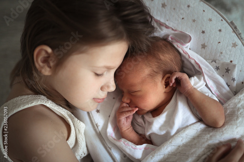 Siblings, Toddler girl gently hugging a newborn, close-up. Concept love and family relationships. Light style and real interior. newborn is sleeping in cocoon.