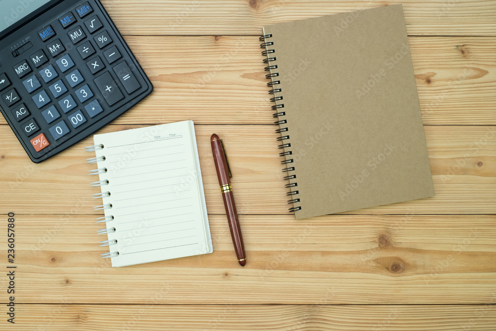 Office supplies or office work essential tools items on wooden desk in workplace, pen with notebook and calculator, top view Office supplies or office work essential tools items on wooden desk in workplace, pen with notebook and calculator, top view