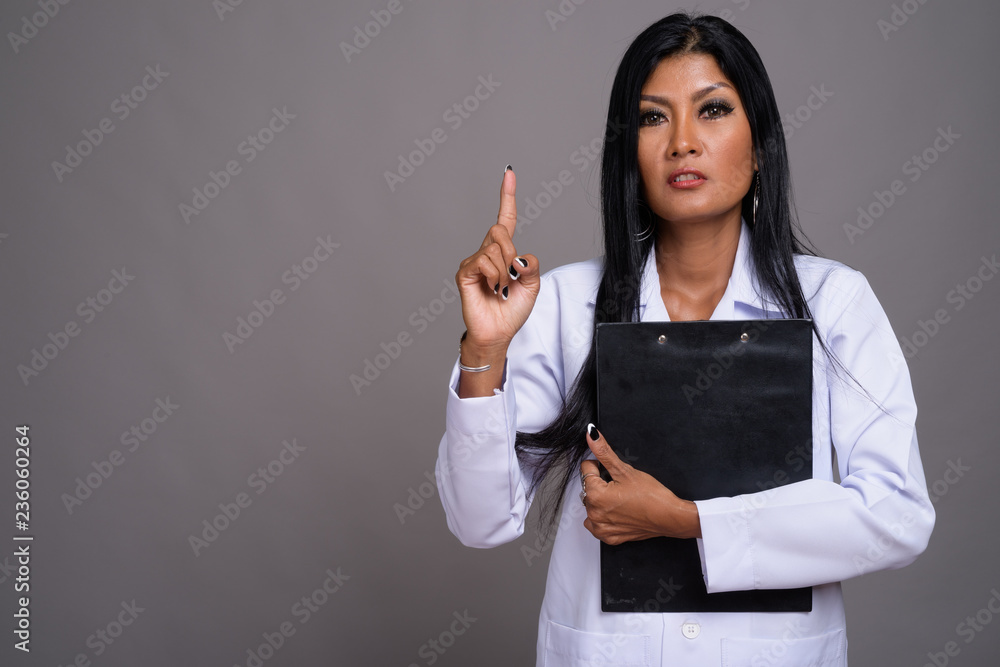 Mature beautiful Asian woman doctor against gray background Mature beautiful Asian woman doctor against gray background
