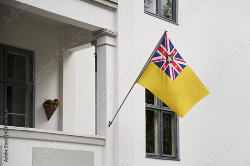 Niue flag hanging on a pole in front of the house. National flag waving on a home displaying on a pole on a front door of a building and raised at a full staff.